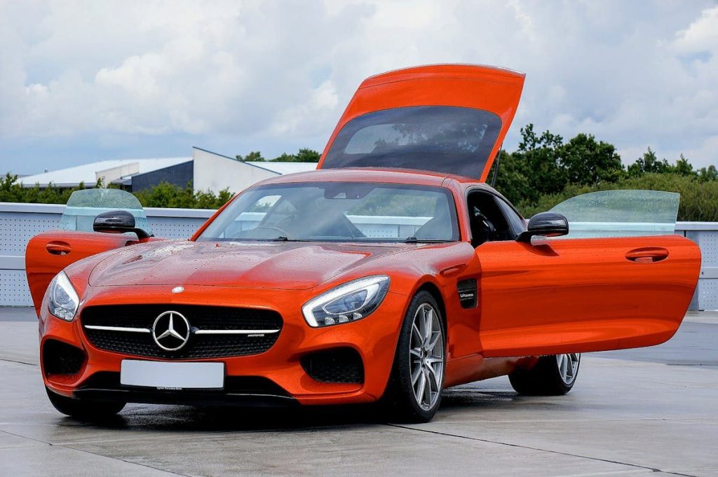 Striking orange sports car displayed outdoors with gullwing doors open, showcasing its design.