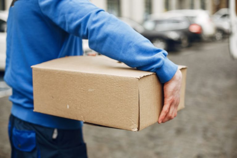 A courier carrying a cardboard box outdoors on a city street, offering delivery service.